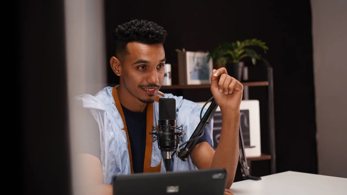 Karanlık stüdyoda mikrofon ve bilgisayarla podcast kaydeden kişi
