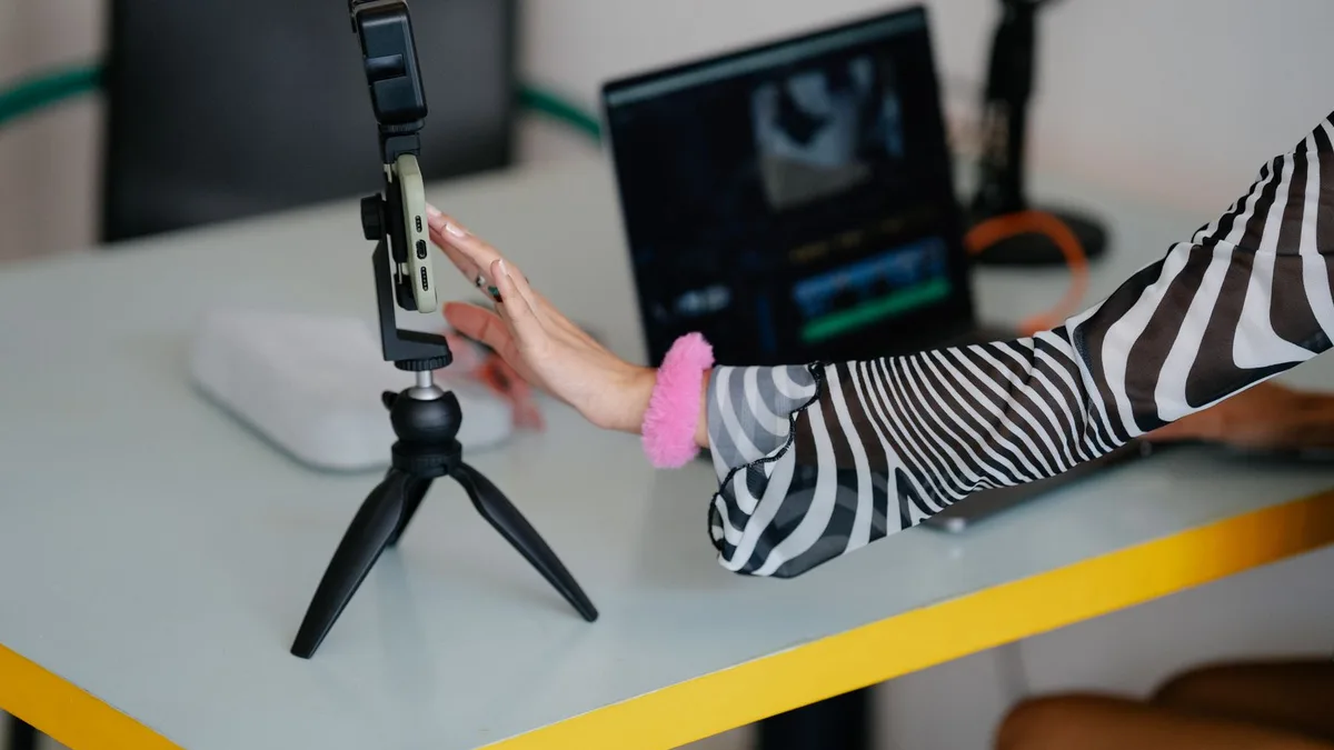 Tripod üzerindeki telefonla masa başında video kaydı hazırlayan kişi