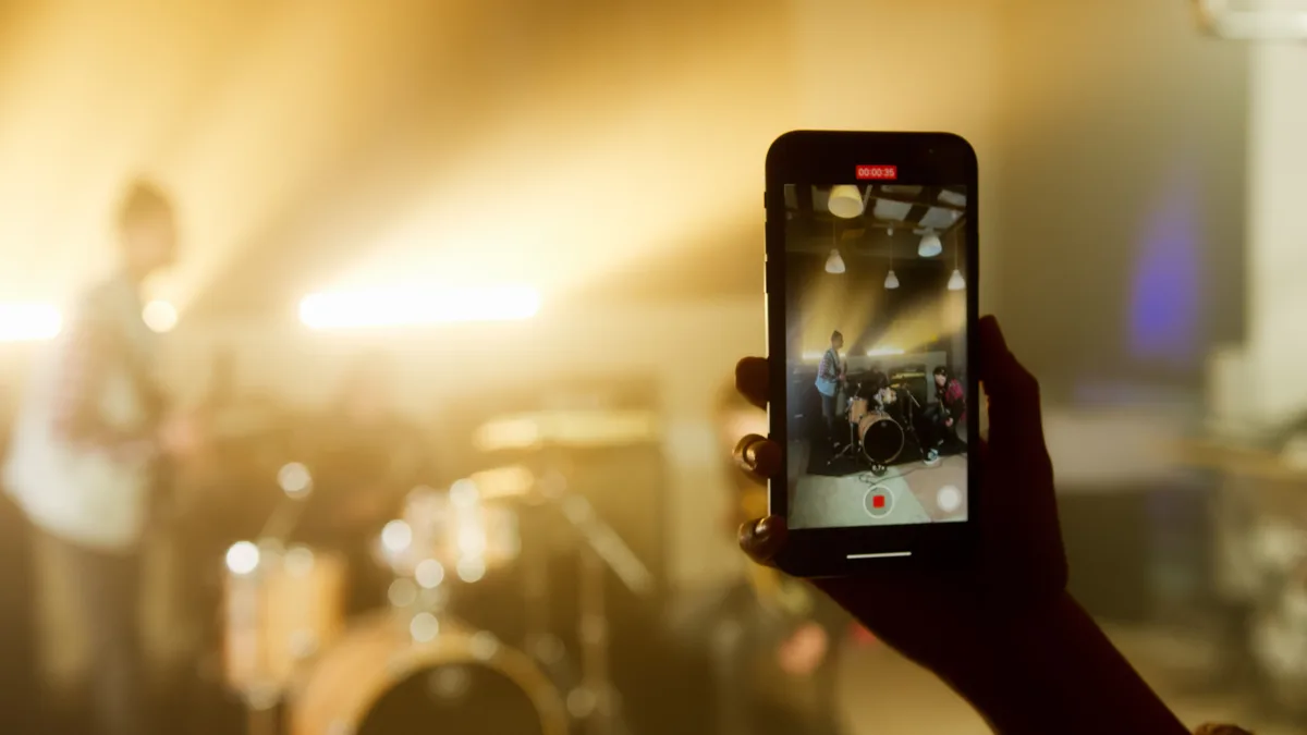 Konser sahnesini dikey telefonla kaydeden bir el