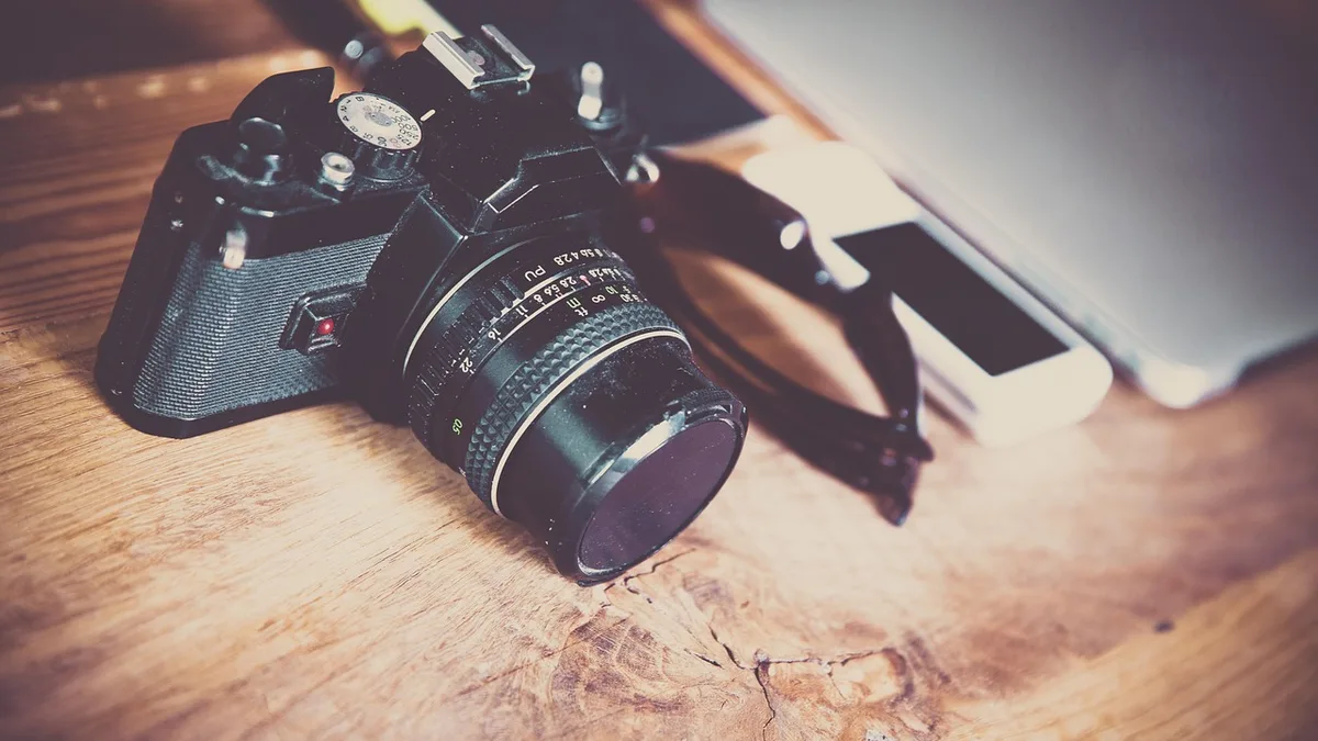 Çalışma masasında fotoğraf makinesi, dizüstü bilgisayar ve not defteri