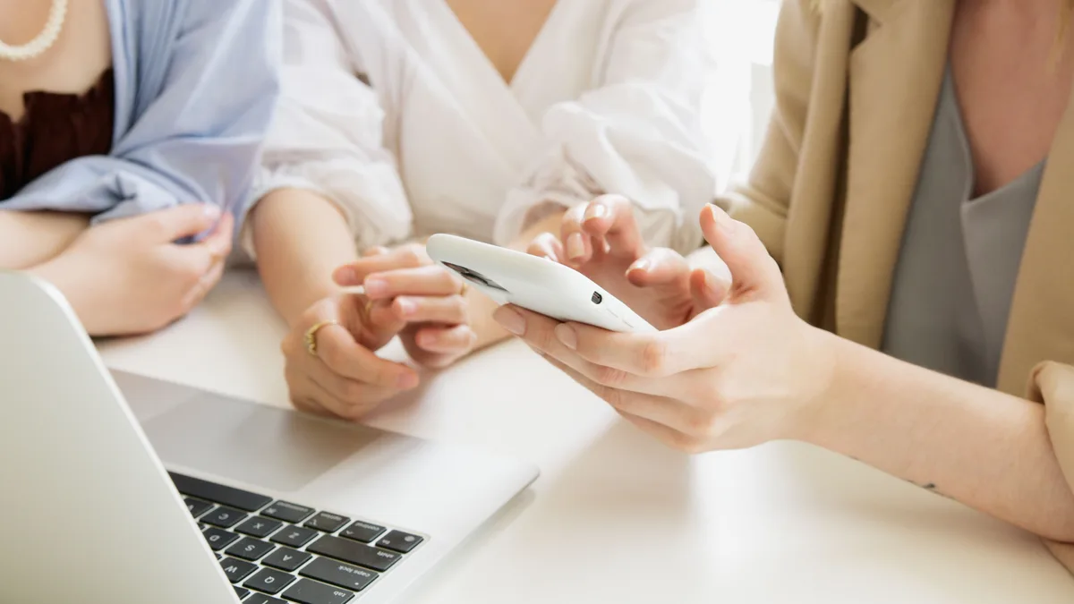 Dizüstü bilgisayar yanında birlikte telefona bakan iki kişi