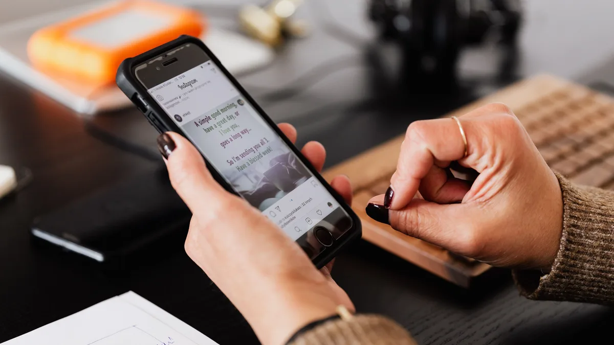 Masa başında telefondaki sosyal medya ekranını inceleyen kişi