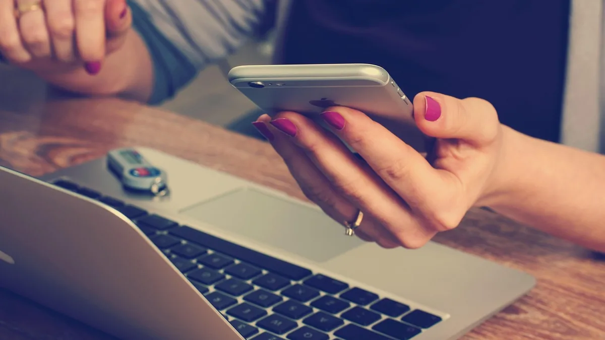 Dizüstü bilgisayar yanında akıllı telefon kullanan kişi