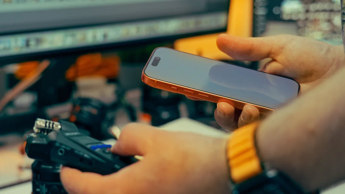 Bilgisayardaki video düzenleme yazılımının yanında telefon ve kamera kullanan kişi