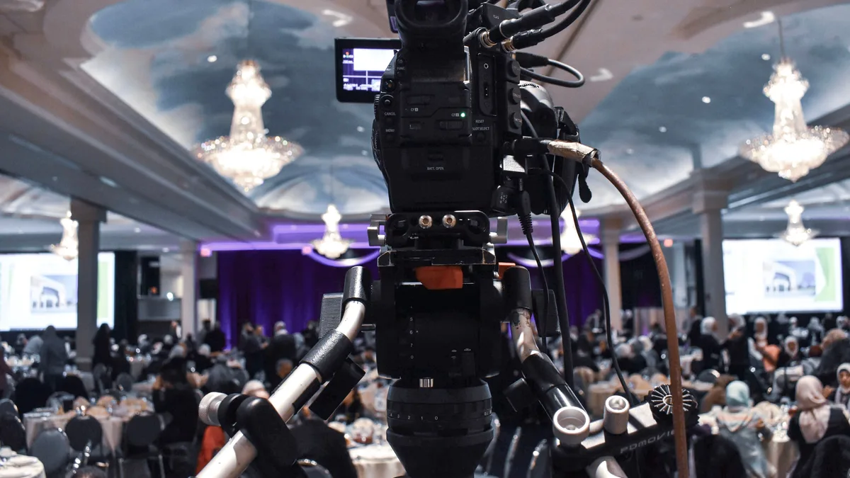 Kalabalık bir salon etkinliğini kaydeden tripod üzerindeki profesyonel kamera