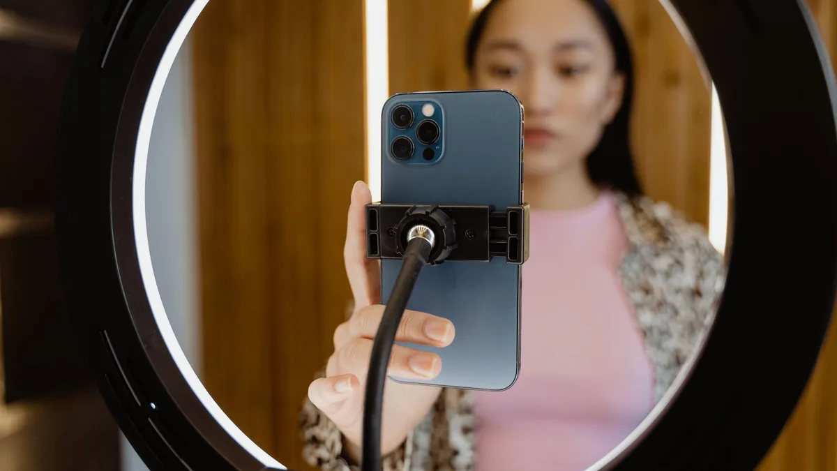 Ring light ortasında tripoda yerleştirilmiş akıllı telefon ve arkasındaki üretici