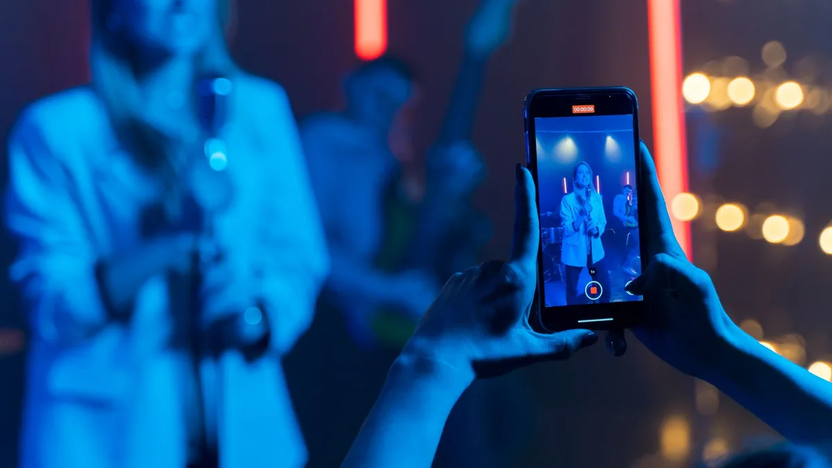 Renkli sahne ışıkları altında dikey telefonla performans kaydı