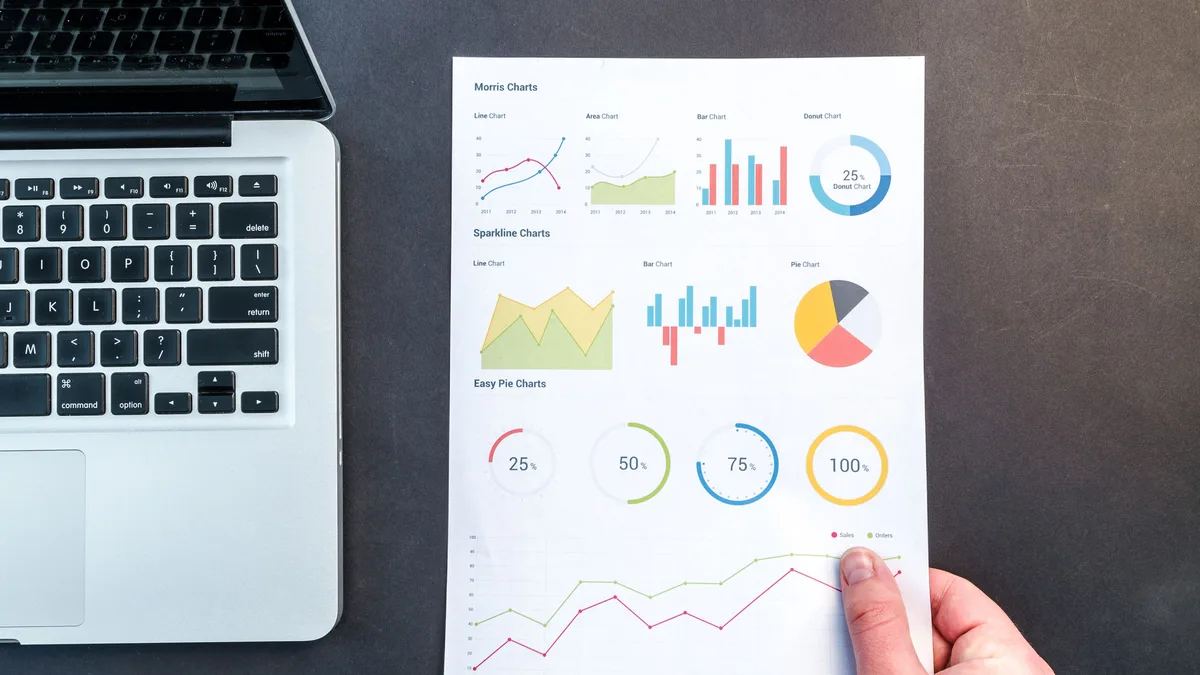 Dizüstü bilgisayar yanında basılı grafik ve tabloları inceleyen el