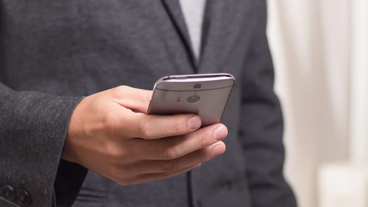 Akıllı telefonunda gelen mesajı dikkatle inceleyen takım elbiseli kişi