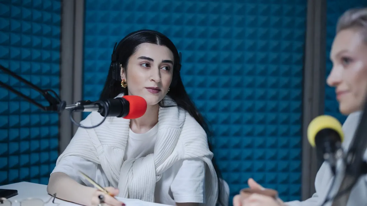 Kayıt stüdyosunda masa mikrofonlarıyla konuşan iki kadın