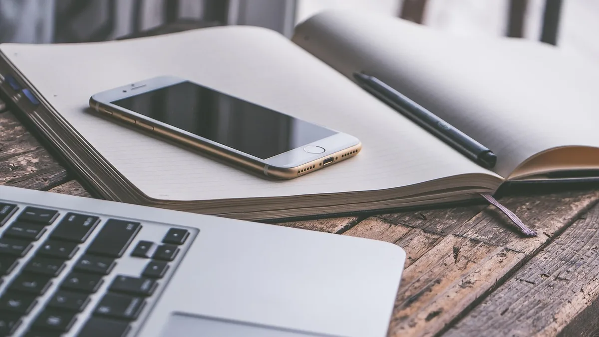 Masa üzerinde telefon, dizüstü bilgisayar ve açık not defteri