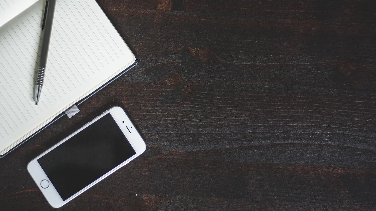 Telefon ve kalemle boş defter üzerinde gelir planı hazırlanabilecek çalışma alanı