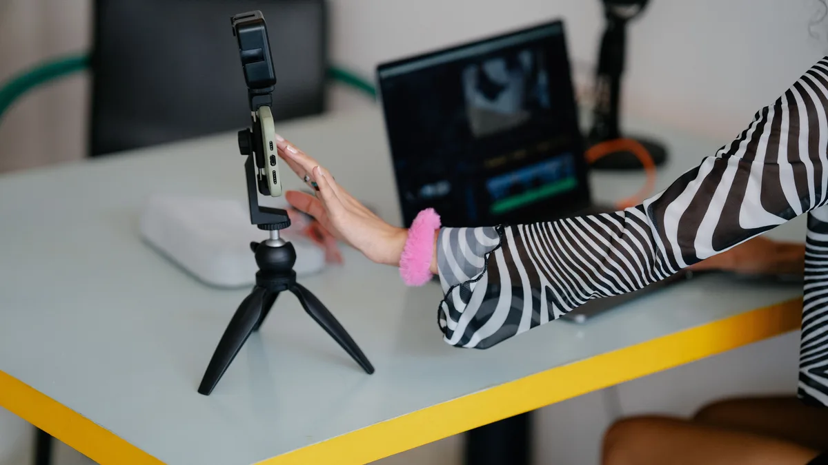 Dizüstü bilgisayar yanında tripod üzerindeki telefonu ayarlayan kadın