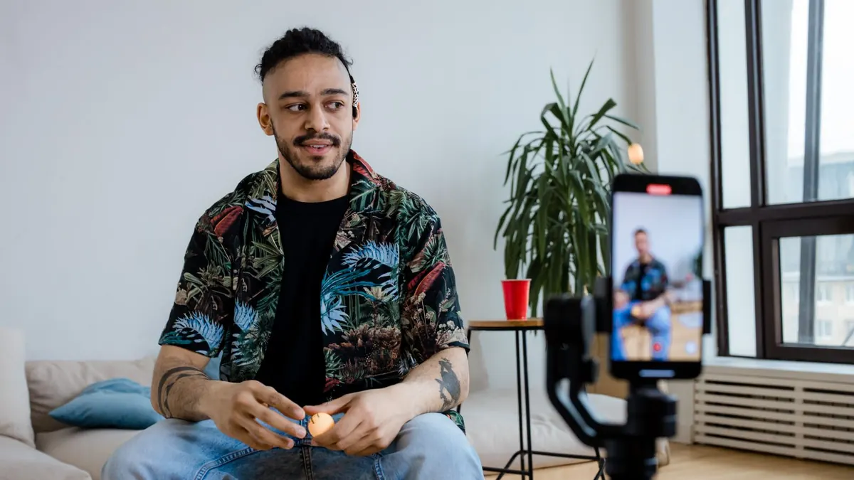 Bir erkek ev ortamında telefon ve tripodla video çekiyor.