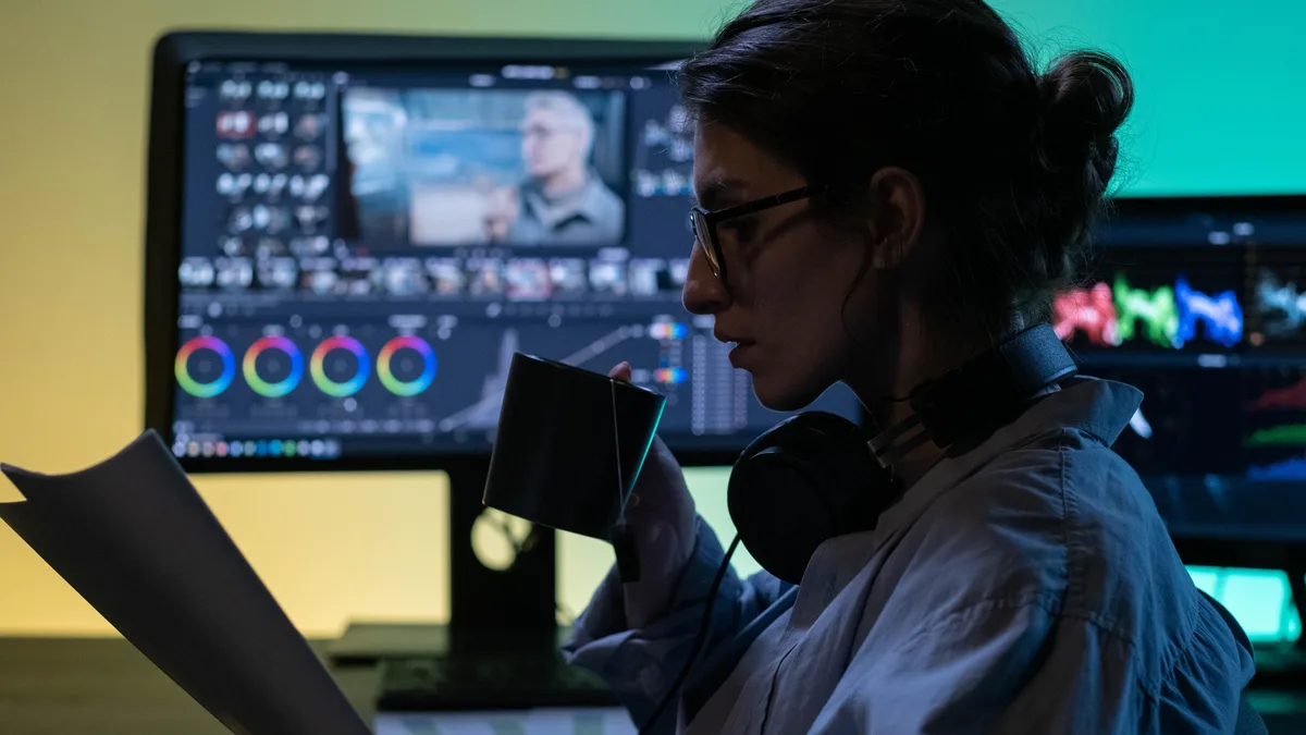 Renk düzenleme monitörleri önünde not kağıdını inceleyen editör