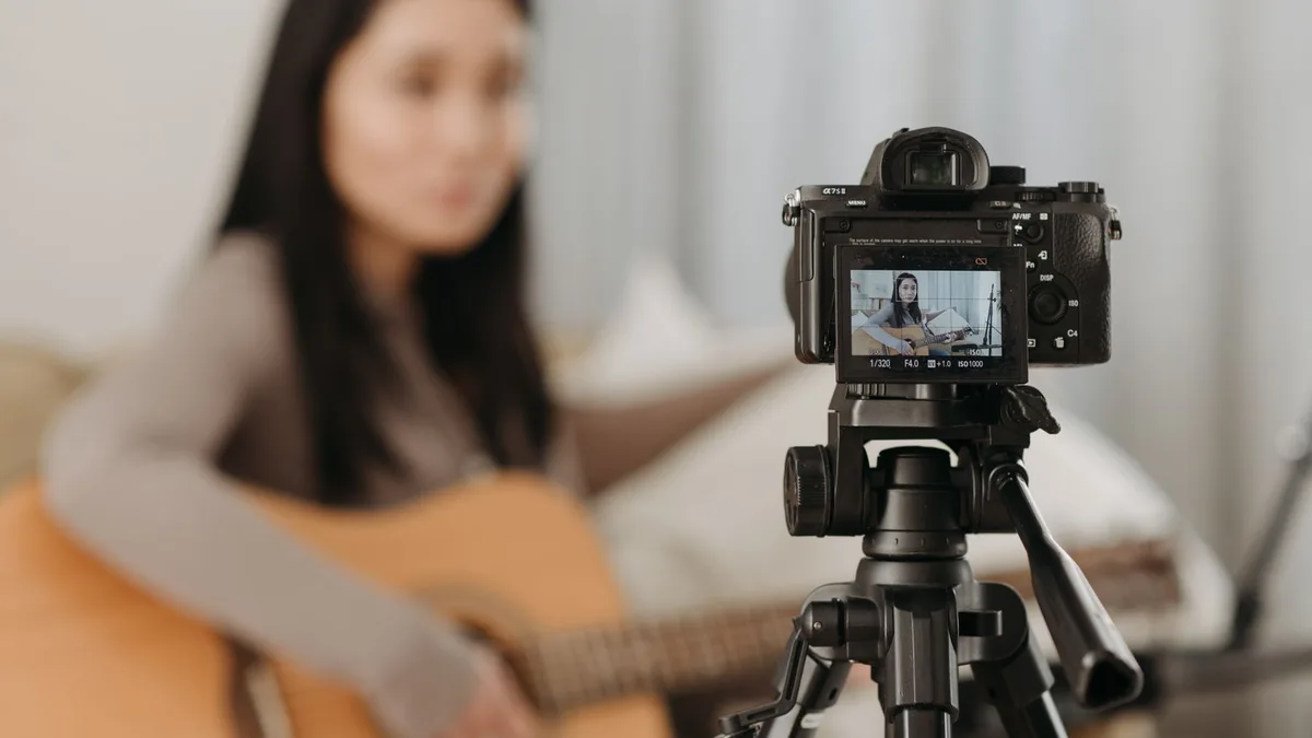Tripod üzerindeki kamerayla gitar çalarken video kaydı yapan kadın