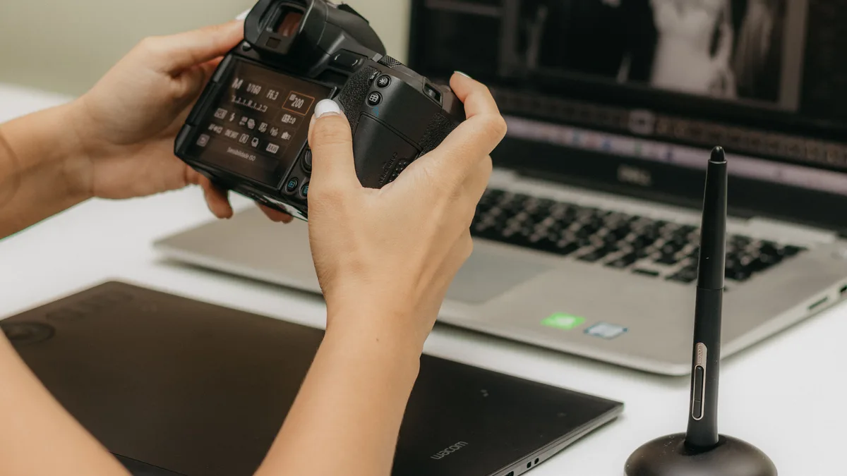 Bilgisayar önünde fotoğraf makinesinin ayarlarını kontrol eden eller