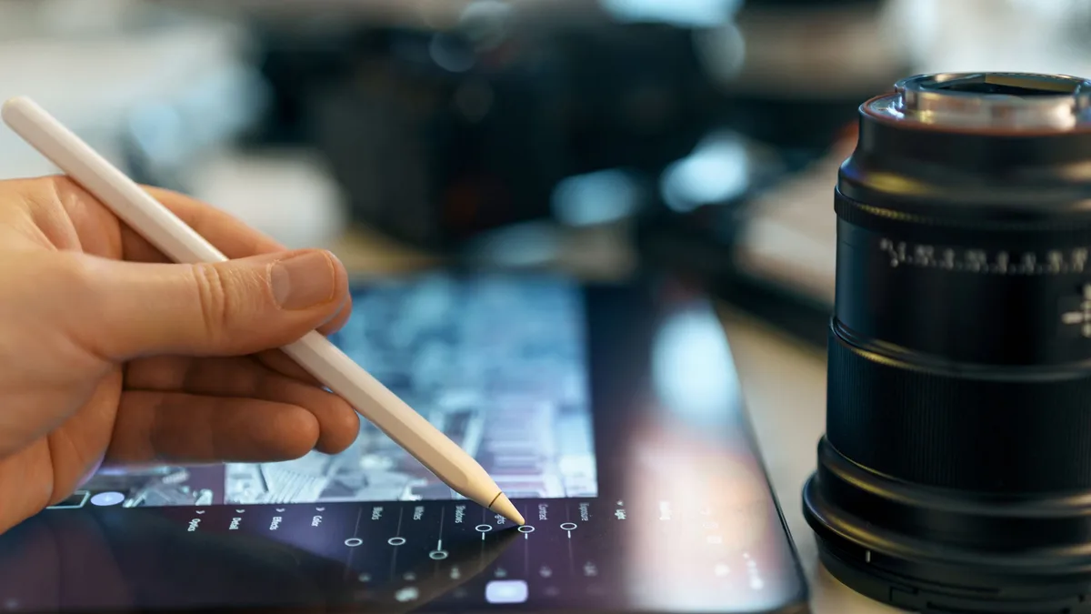 Grafik tablet üzerinde kalemle çalışan bir kişinin eli ve kamera lensi