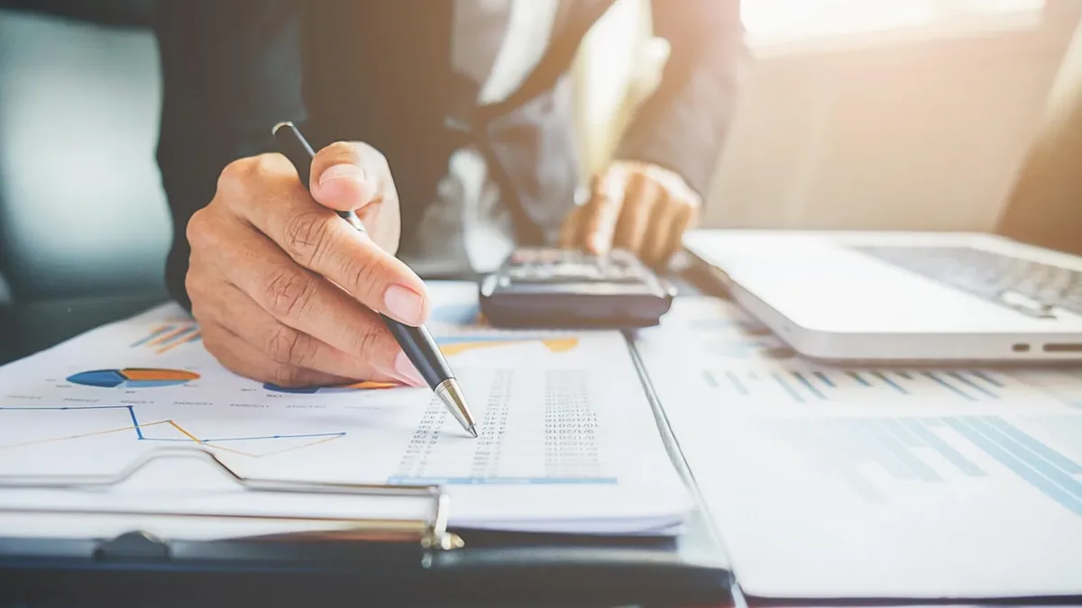Finansal belgeleri kalem ve hesap makinesiyle inceleyen kişi