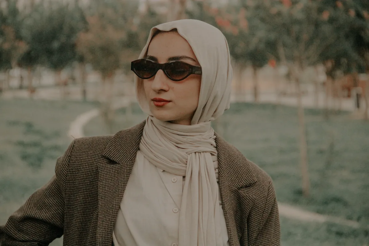 Güneş gözlüğü ve nötr tonlarda tesettür kombini kullanan kadın