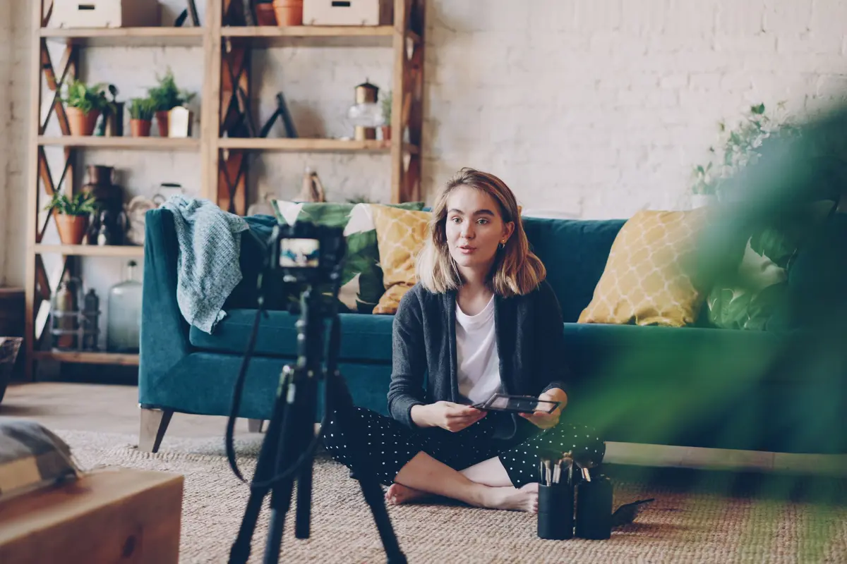 Oturma odasında tripod üzerindeki kamerayla kendini kaydeden kadın