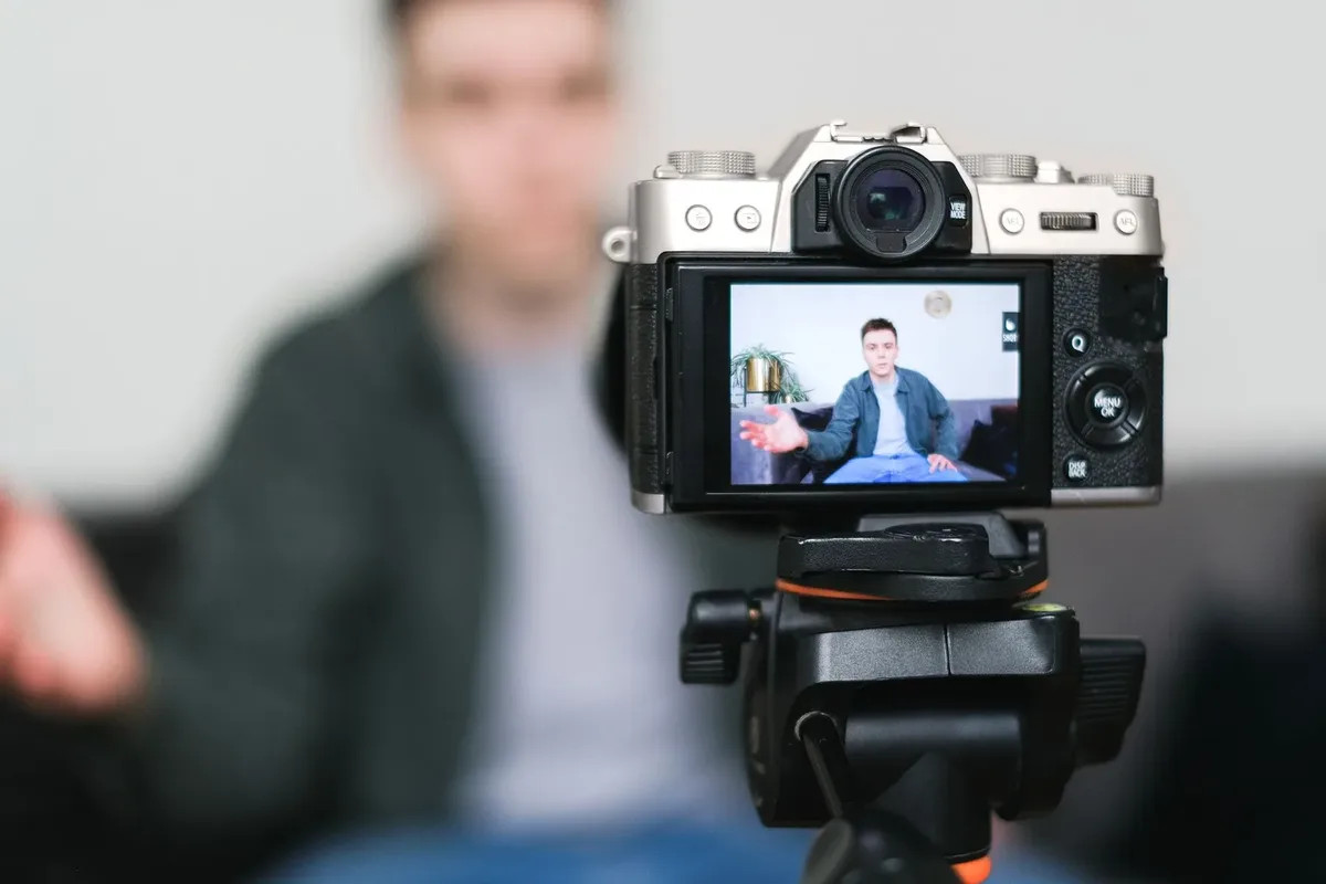 Tripod üzerindeki kameraya konuşarak ürün videosu çeken kişi