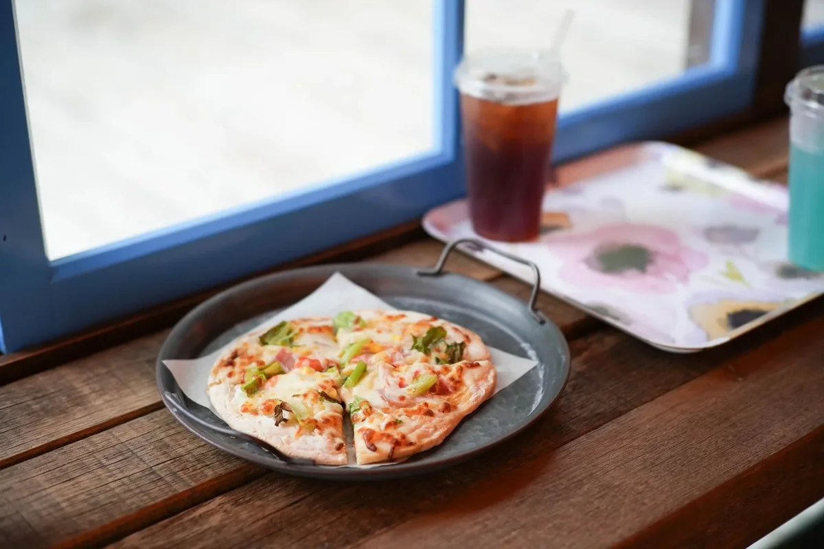 Pencere yanında pizza ve soğuk içecek bulunan masa